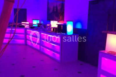 Scène de DJ éclairée par des lumières colorées, entourée de rideaux rouges et de haut-parleurs dans une salle.