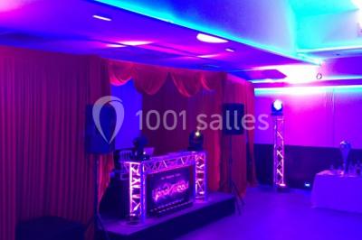 Scène de DJ éclairée par des lumières colorées, entourée de rideaux rouges et de haut-parleurs dans une salle.