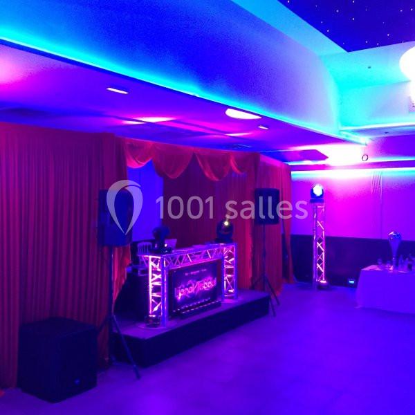 Scène de DJ éclairée par des lumières colorées, entourée de rideaux rouges et de haut-parleurs dans une salle.