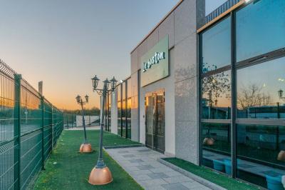 Salle intérieure avec terrain de sport entouré de filets, tables et chaises disposées sur un sol en gazon synthétique.