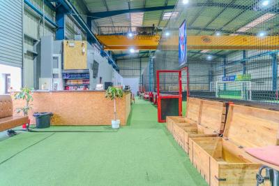 Salle intérieure avec terrain de sport entouré de filets, tables et chaises disposées sur un sol en gazon synthétique.
