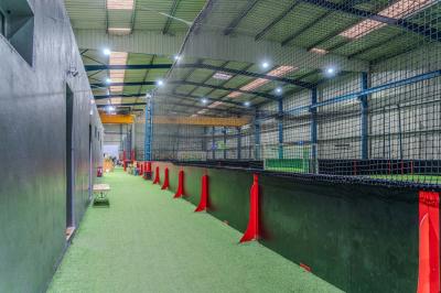 Salle intérieure avec terrain de sport entouré de filets, tables et chaises disposées sur un sol en gazon synthétique.