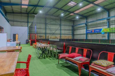 Salle intérieure avec terrain de sport entouré de filets, tables et chaises disposées sur un sol en gazon synthétique.