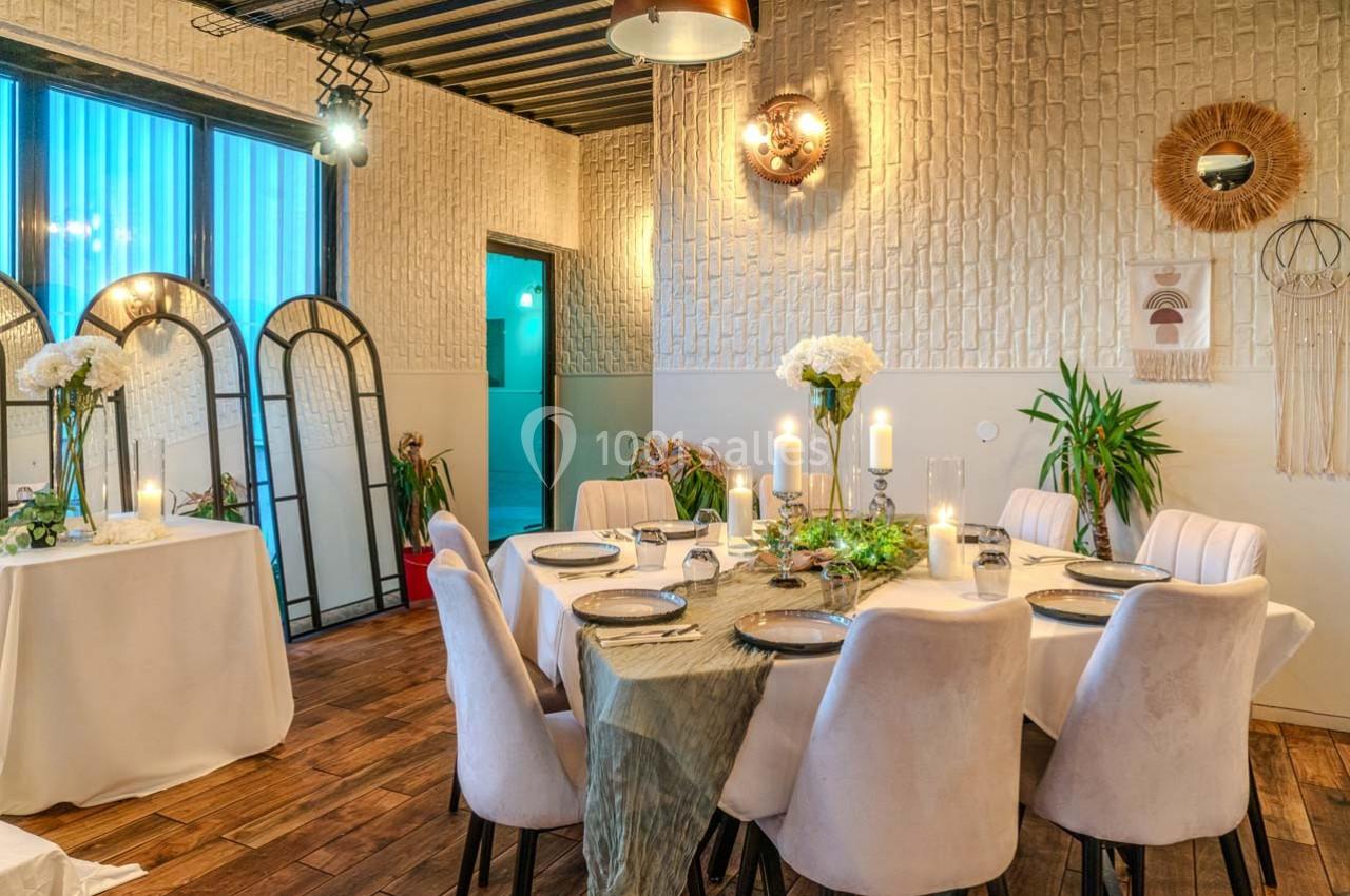 Salle à manger élégante avec table dressée, chaises blanches, décorations murales et lumière tamisée.