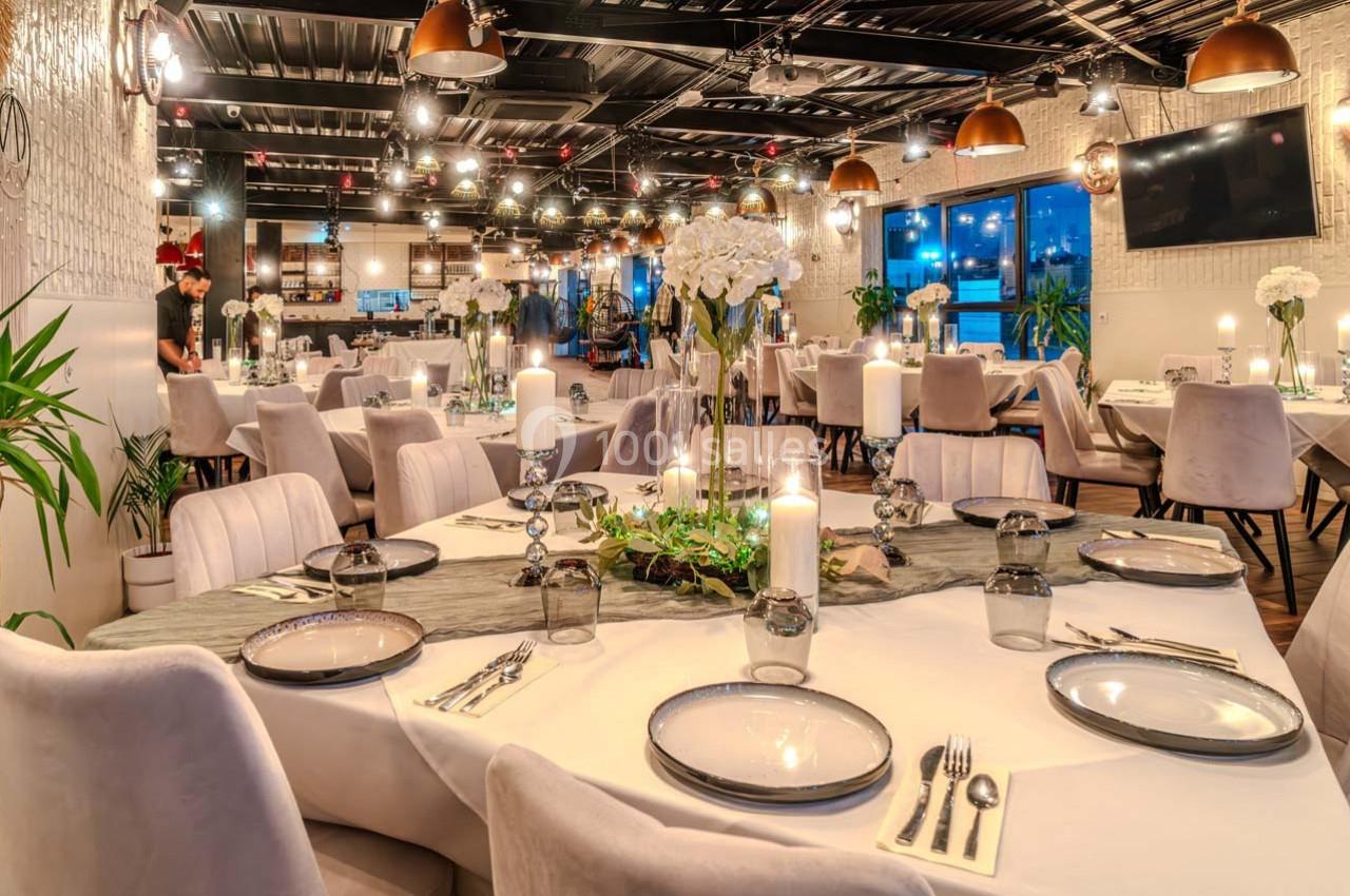 Salle de restaurant élégante avec tables dressées, chandeliers, fleurs blanches et éclairage chaleureux.
