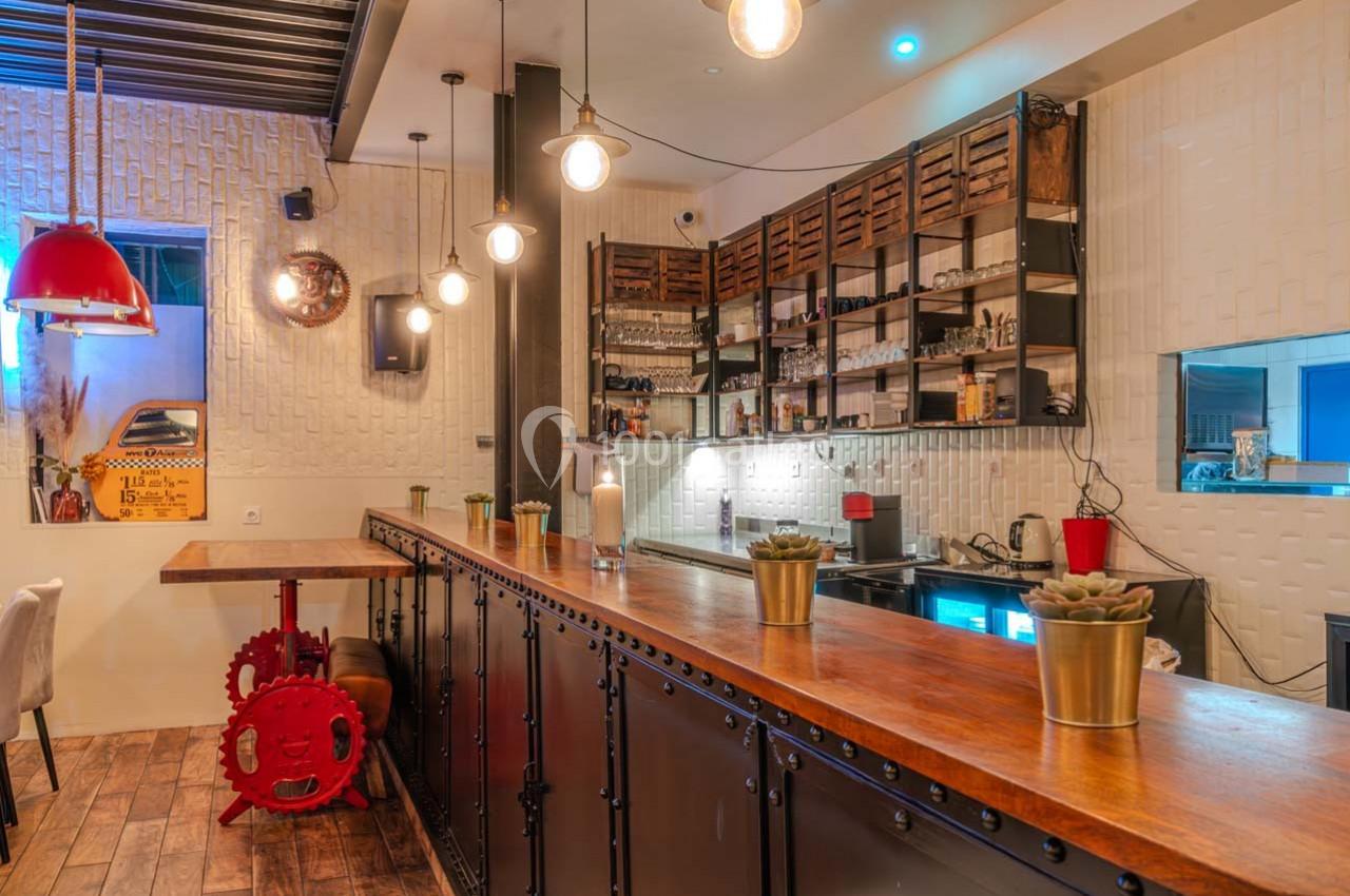 Intérieur d'un café avec un comptoir en bois, étagères murales, suspensions lumineuses et décor industriel.