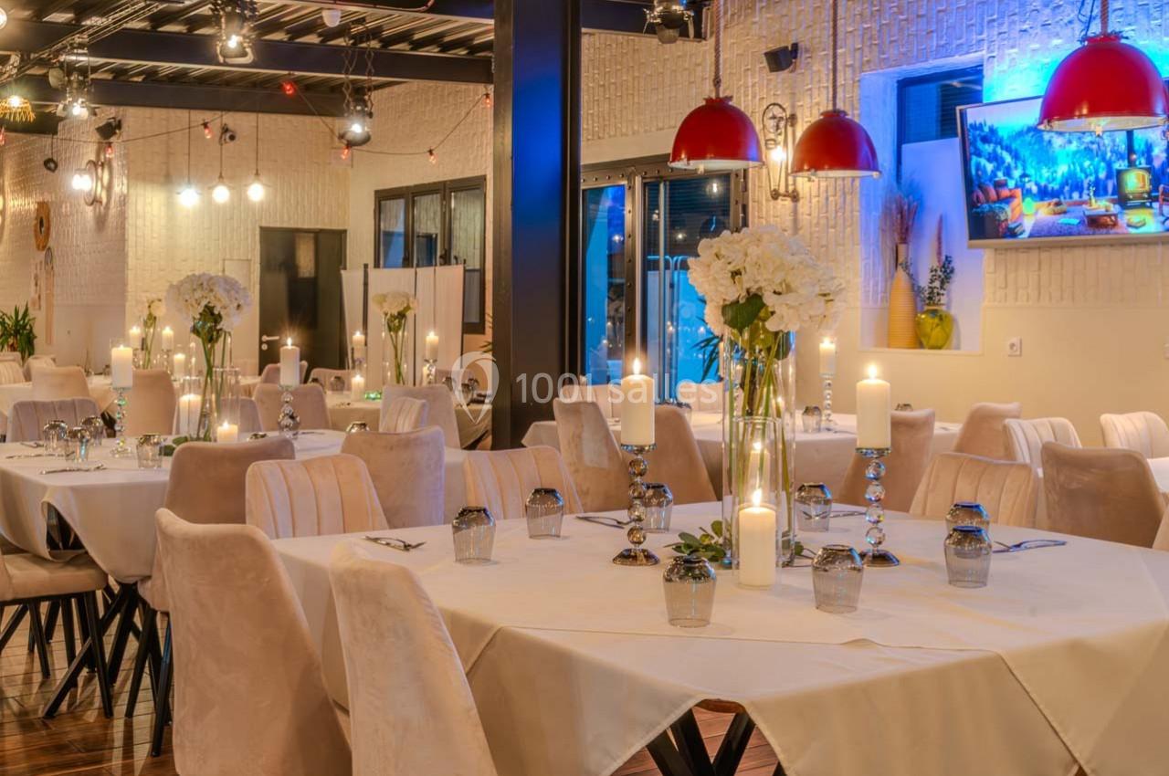 Salle de restaurant élégante avec tables dressées, chandeliers, fleurs blanches et éclairage chaleureux.