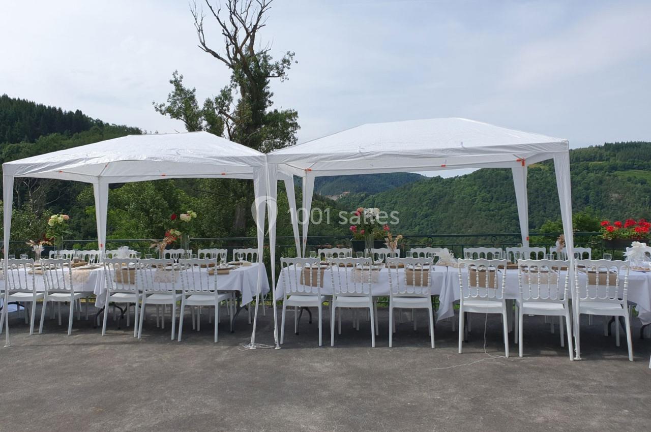 Deux tonnelles blanches abritent des tables dressées pour un repas en extérieur, avec vue sur un paysage vallonné.