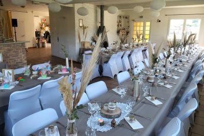 Tables dressées pour un repas en extérieur devant une maison en pierre et crépi, avec une borne photo à gauche.