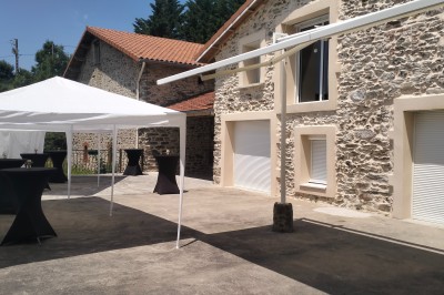Tables dressées pour un repas en extérieur devant une maison en pierre et crépi, avec une borne photo à gauche.