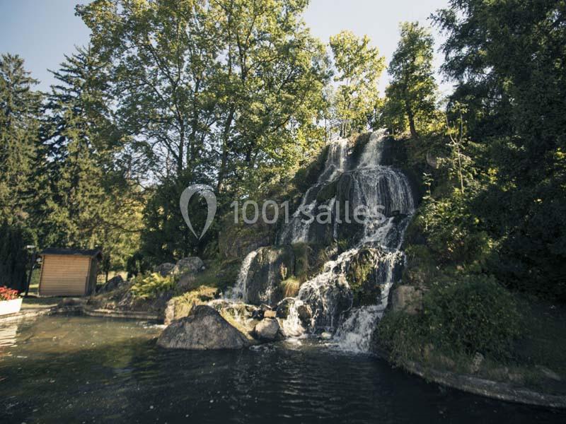 Cascade entourée de végétation, tombant sur des rochers dans un petit bassin d'eau en pleine nature.