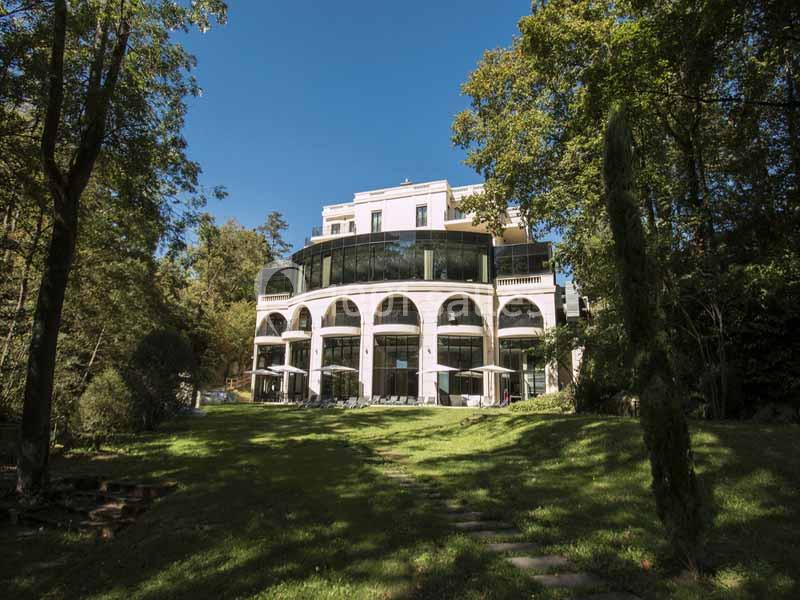 Façade d'un bâtiment moderne entouré de verdure, avec une pelouse et des arbres sous un ciel dégagé.