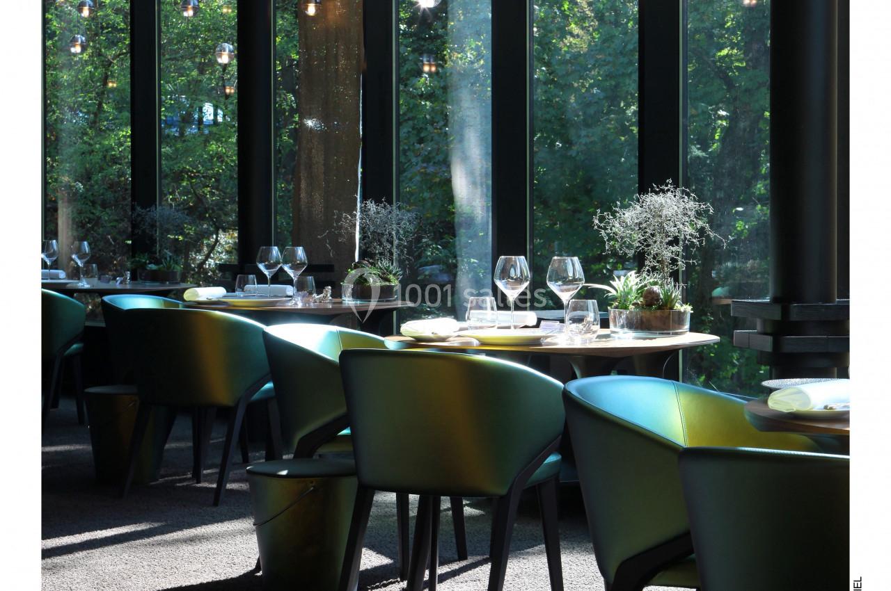 Salle de restaurant lumineuse avec de grandes baies vitrées, des tables dressées et des suspensions en verre.
