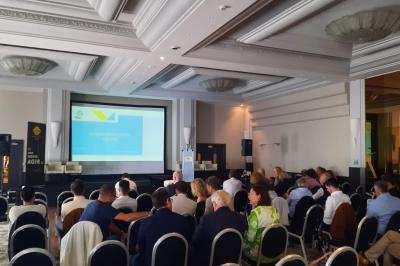Un public assis dans une salle de conférence, attentif à une présentation sur une scène éclairée.
