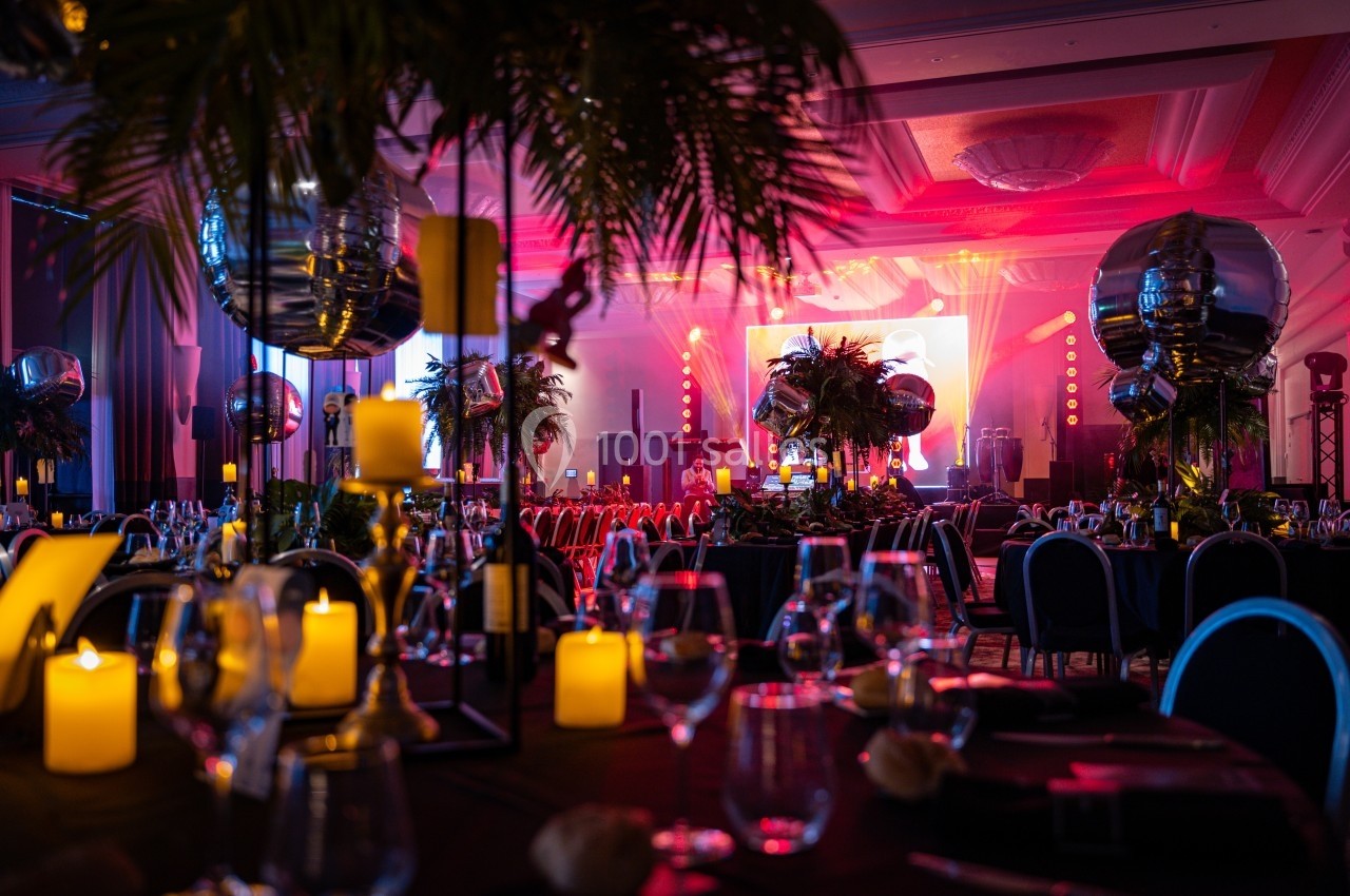 Salle de réception décorée avec des bougies, des plantes et des ballons, éclairée par des lumières colorées.