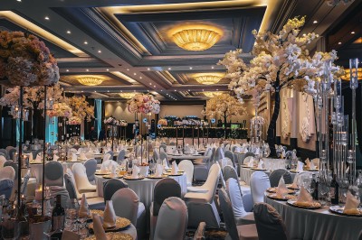 Des invités dînent autour de tables rondes tandis qu'un groupe joue sur une scène illuminée dans une salle de réception.