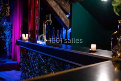 Comptoir de bar sombre avec des bougies allumées, décoré de motifs floraux et éclairé par une lumière tamisée.