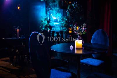 Comptoir de bar sombre avec des bougies allumées, décoré de motifs floraux et éclairé par une lumière tamisée.