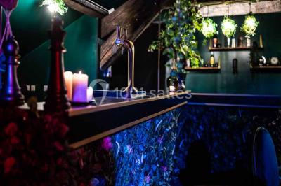 Comptoir de bar sombre avec des bougies allumées, décoré de motifs floraux et éclairé par une lumière tamisée.