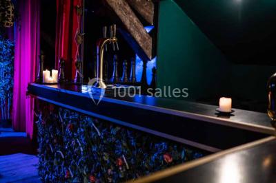 Comptoir de bar sombre avec des bougies allumées, décoré de motifs floraux et éclairé par une lumière tamisée.