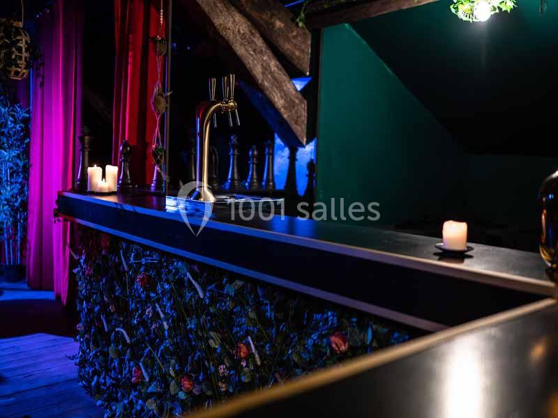 Comptoir de bar sombre avec des bougies allumées, décoré de motifs floraux et éclairé par une lumière tamisée.