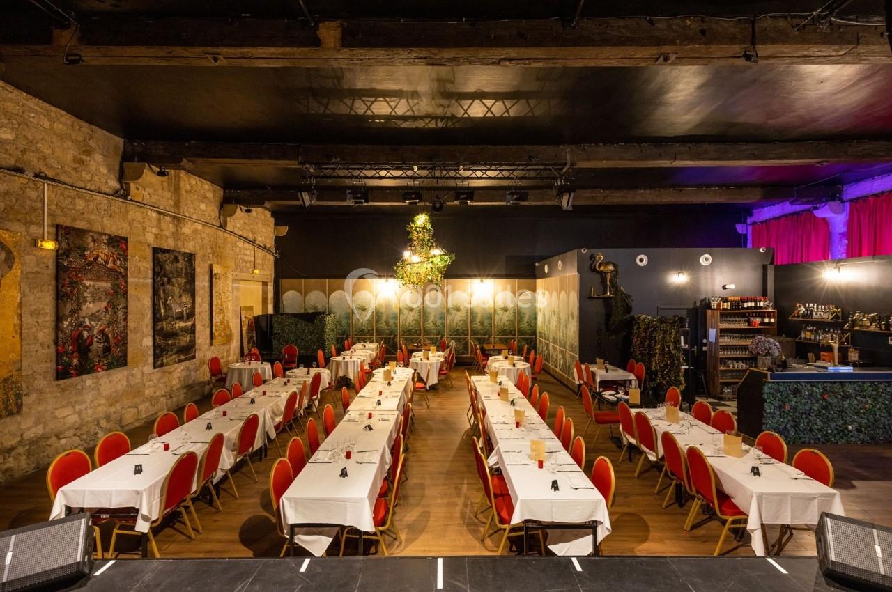 Salle de réception avec tables alignées, nappes blanches, chaises rouges et décorations murales dans une ambiance…