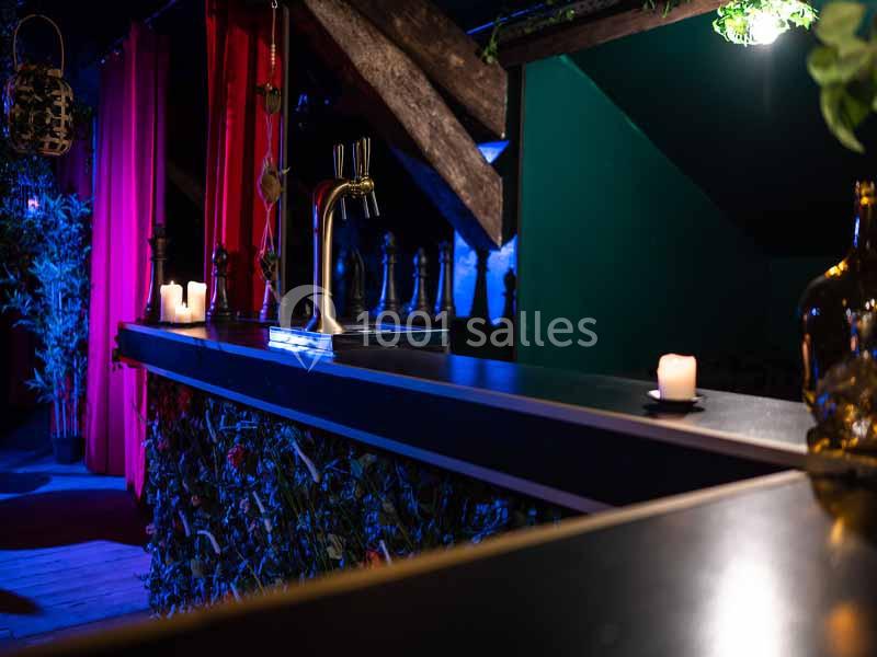 Comptoir de bar avec une tireuse à bière, éclairage tamisé, bougies allumées et décor végétal en arrière-plan.