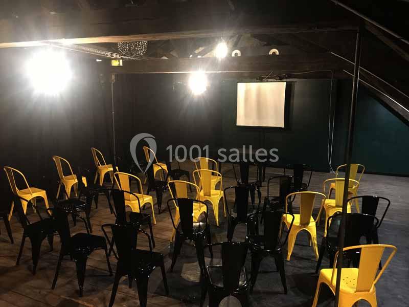 Salle sombre avec des chaises jaunes et noires disposées face à un écran de projection blanc.