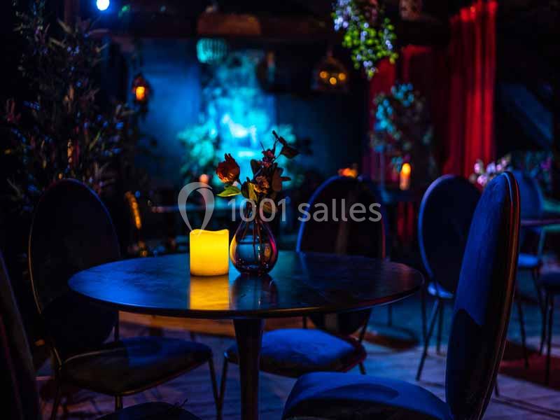 Table ronde avec une bougie allumée et un vase de fleurs, dans une ambiance tamisée et décor sombre.