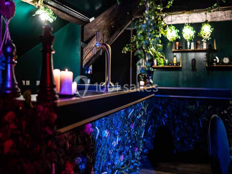 Bar décoré de plantes, bougies et éclairage tamisé, avec un robinet de bière en métal sur le comptoir.