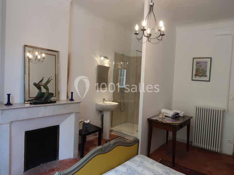 Chambre avec cheminée, lit, table, et salle de bain attenante équipée d'une douche et d'un lavabo.
