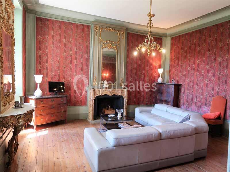 Salon élégant avec canapé blanc, cheminée ornée, lustre doré, murs rouges décorés et mobilier classique en bois.