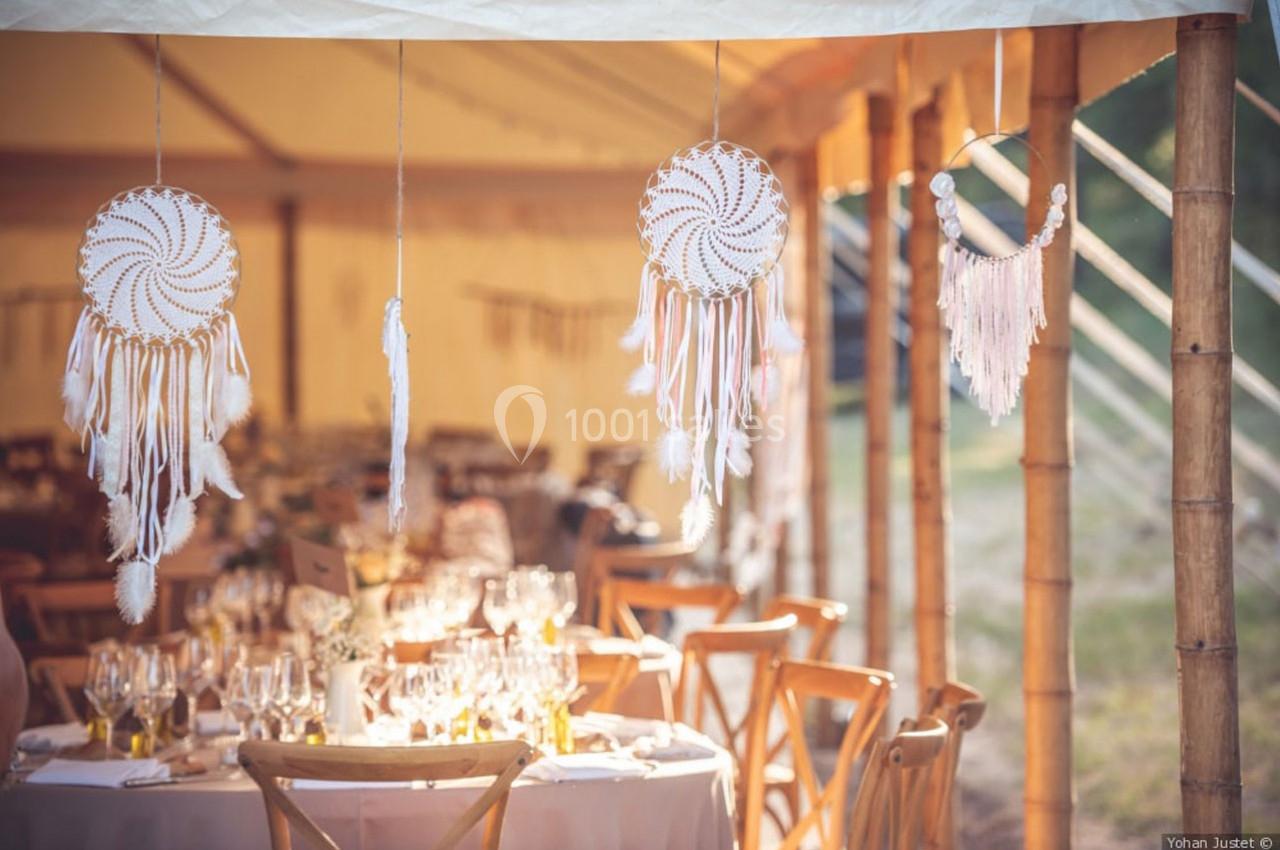 Décoration de mariage avec attrape-rêves suspendus et tables dressées sous une tente lumineuse en bambou.
