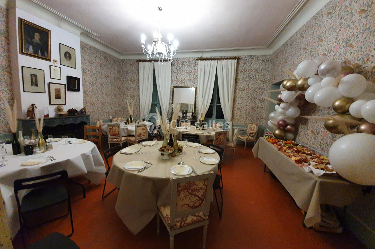 Salle décorée pour un événement, avec tables dressées, guirlandes de ballons et buffet sur le côté.