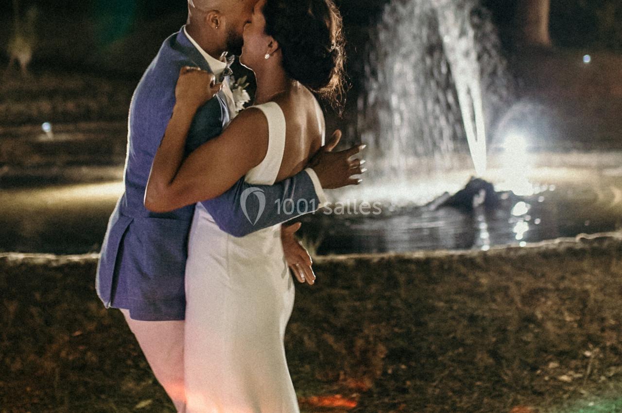Un couple danse tendrement le soir près d'une fontaine illuminée dans un cadre extérieur.