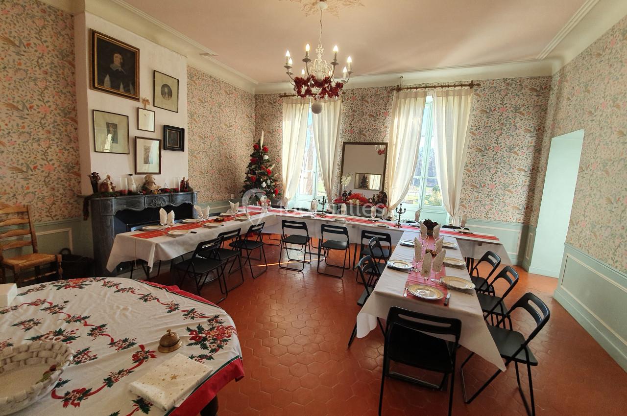 Salle à manger décorée pour Noël avec une grande table dressée, un sapin et des murs ornés de papier peint floral.
