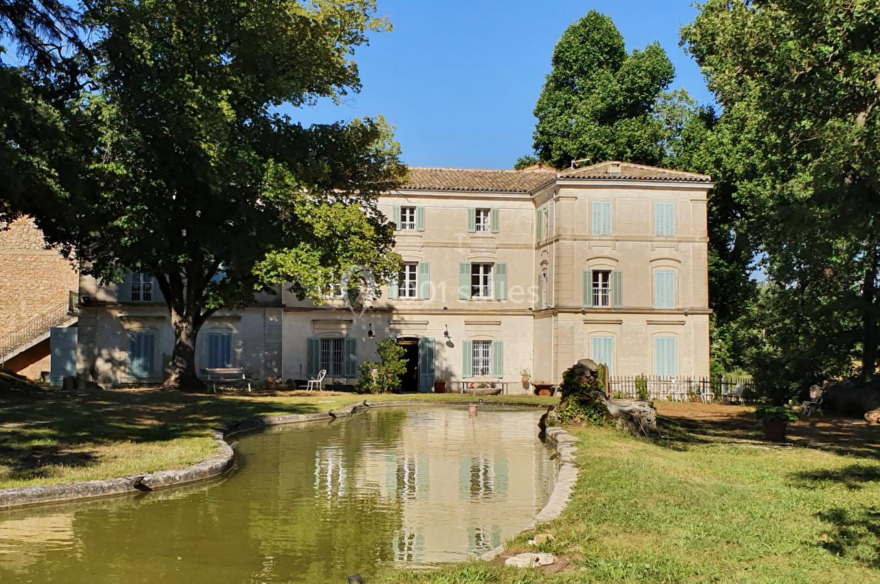 Façade d'un bâtiment ancien entouré d'arbres, avec un petit plan d'eau au premier plan.