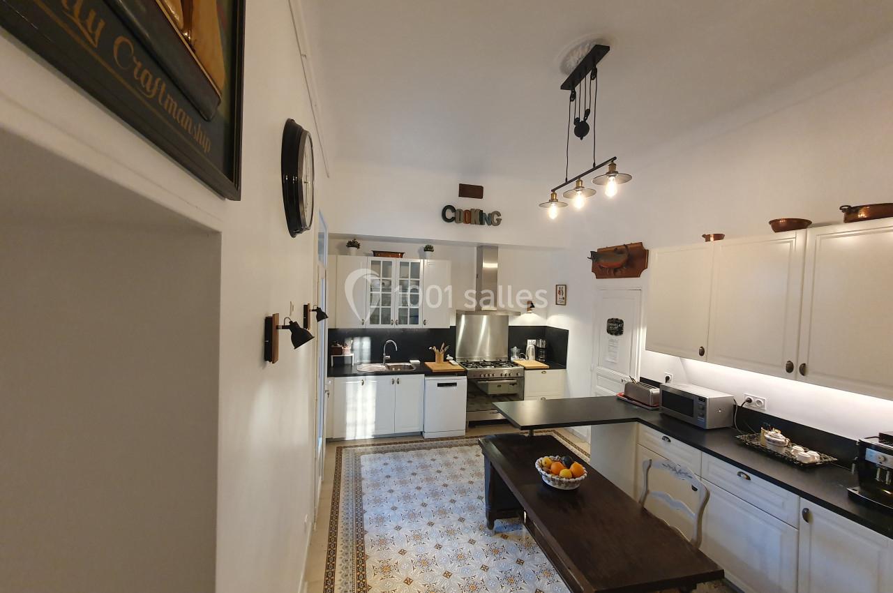 Cuisine lumineuse avec meubles blancs, plan de travail noir, table en bois, et sol à motifs décoratifs.