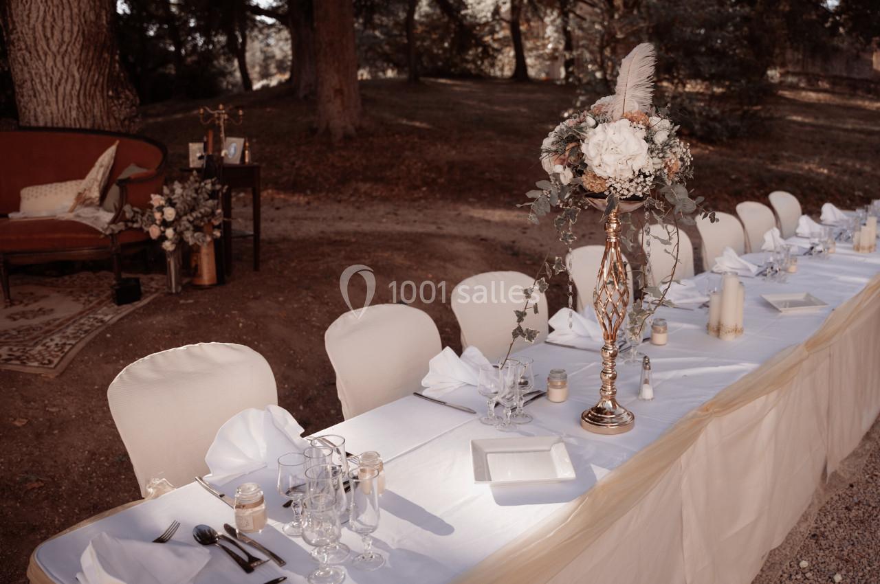 Table de réception en extérieur, décorée de nappes blanches, chandeliers, fleurs et vaisselle élégante.
