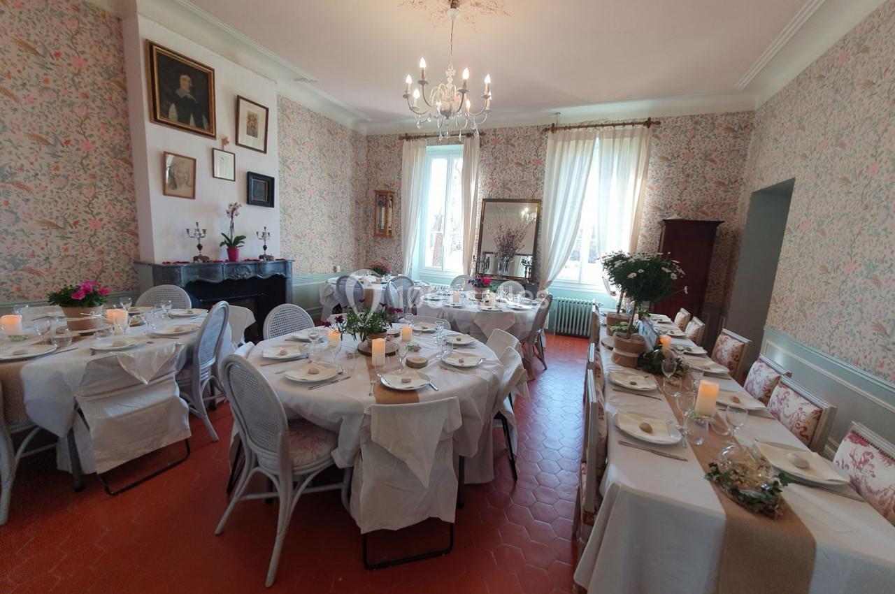 Salle à manger décorée avec des tables dressées pour un repas, éclairée par des fenêtres et un lustre.