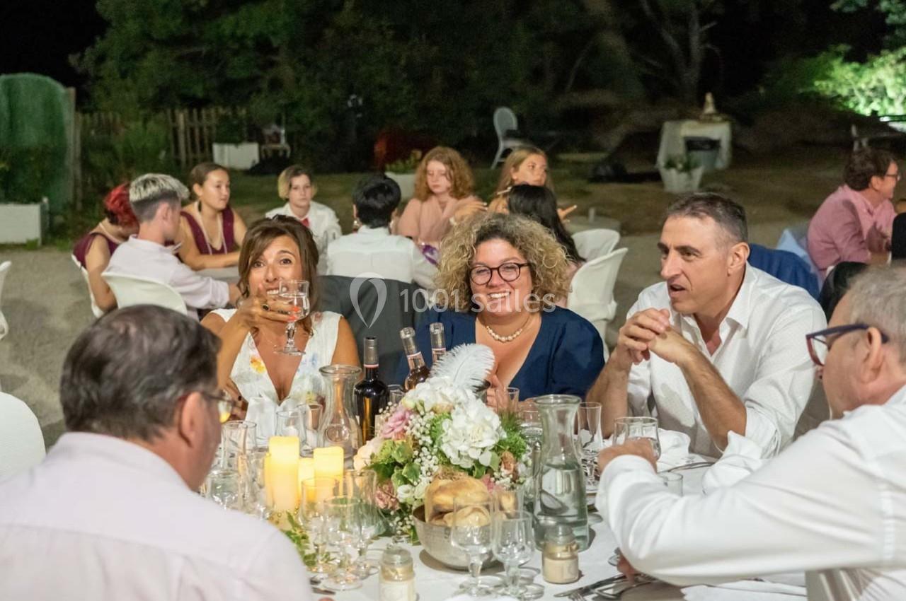 Des convives assis autour d'une table décorée, partageant un repas en extérieur lors d'une soirée festive.