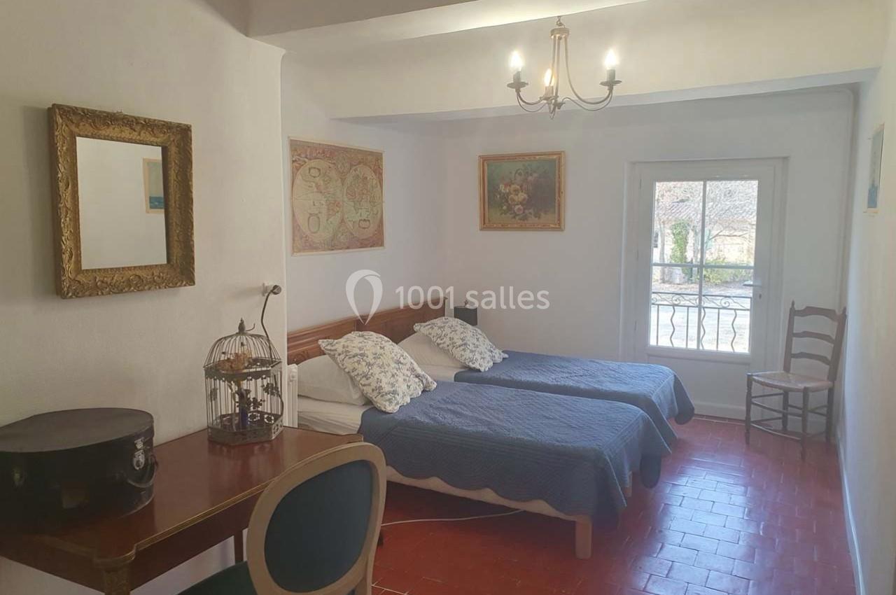 Chambre avec deux lits simples, bureau, chaise, miroir, décoration murale et fenêtre donnant sur un balcon.