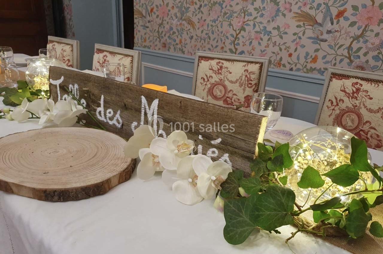 Table décorée pour un mariage avec une pancarte en bois, des orchidées blanches, du lierre et des guirlandes lumineuses.