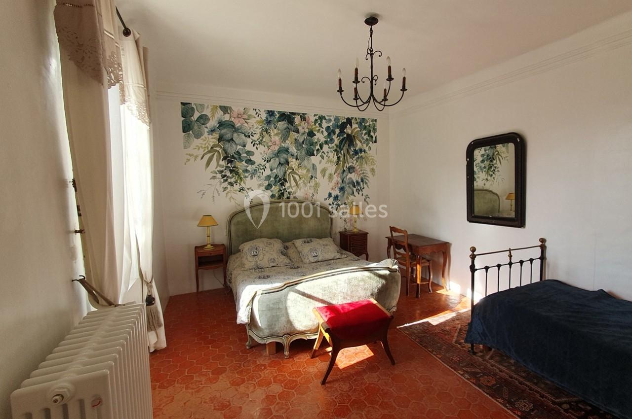 Chambre lumineuse avec un lit double, un lit simple, un bureau, un miroir et une décoration murale florale.