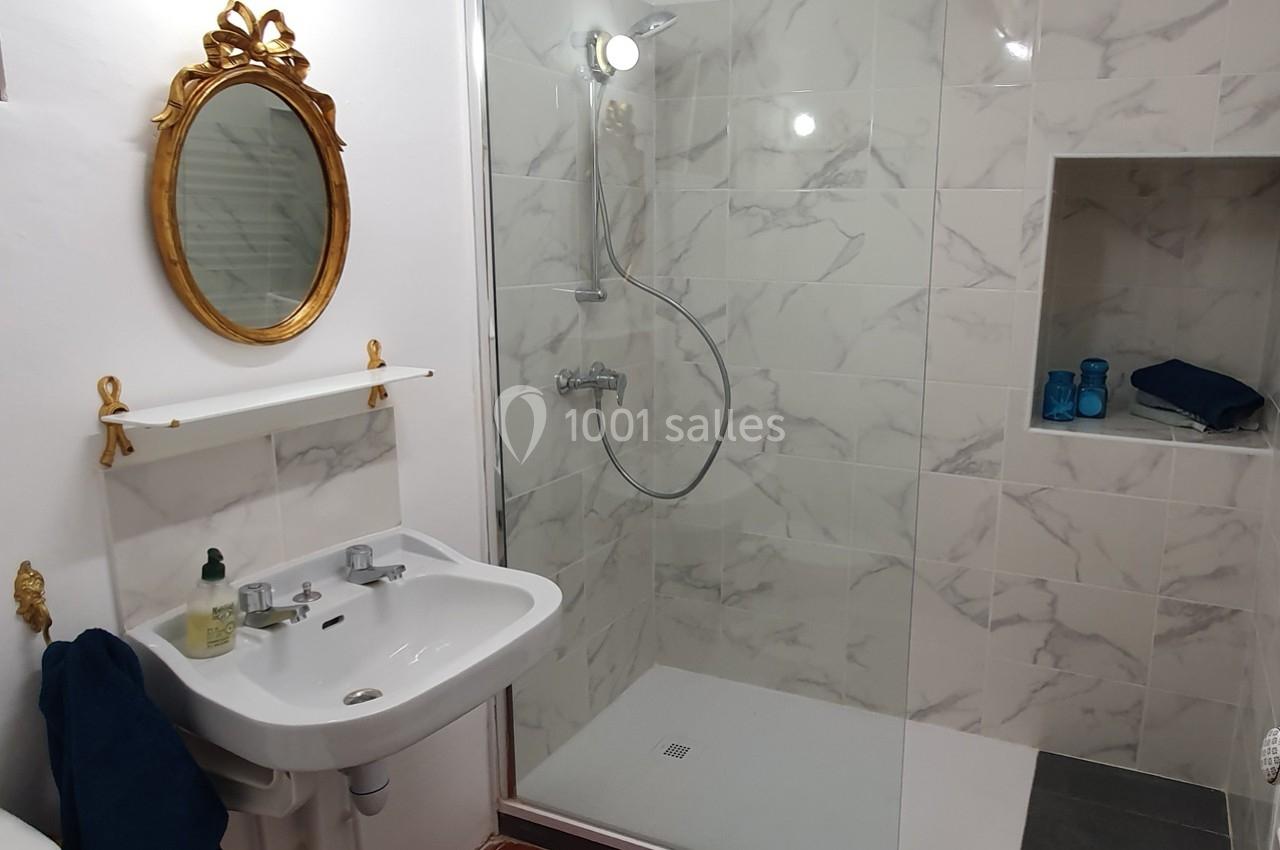 Salle de bain avec douche à l'italienne, lavabo avec miroir doré et étagère, carrelage effet marbre.