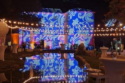 Façade d'un bâtiment illuminée par des motifs colorés, avec guirlandes lumineuses et leur reflet dans un plan d'eau.