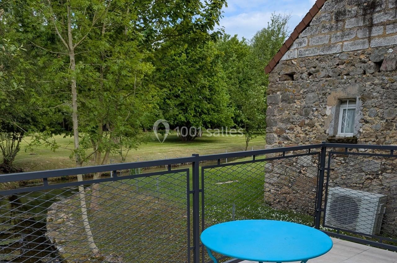 Vue depuis une terrasse avec table bleue, donnant sur un jardin verdoyant et un bâtiment en pierre.