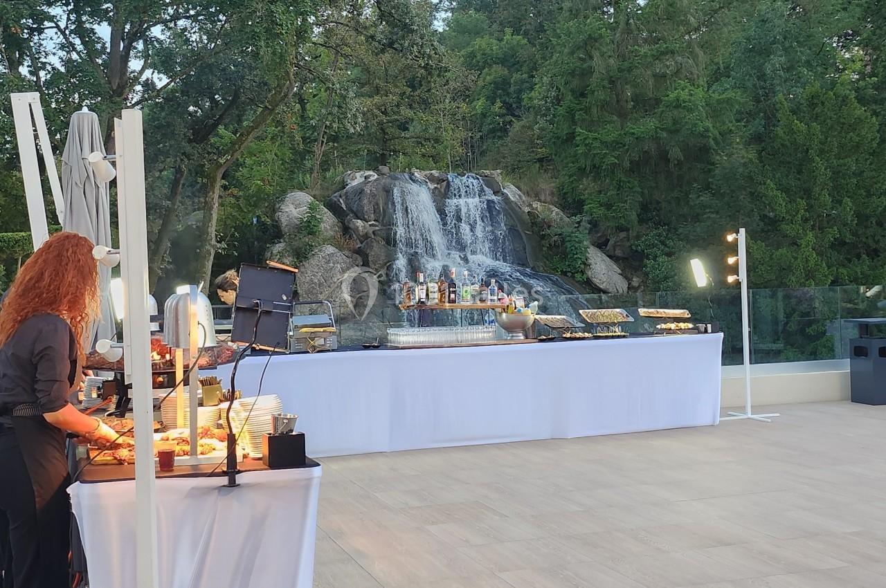 Buffet en plein air avec des tables dressées devant une cascade entourée de végétation.