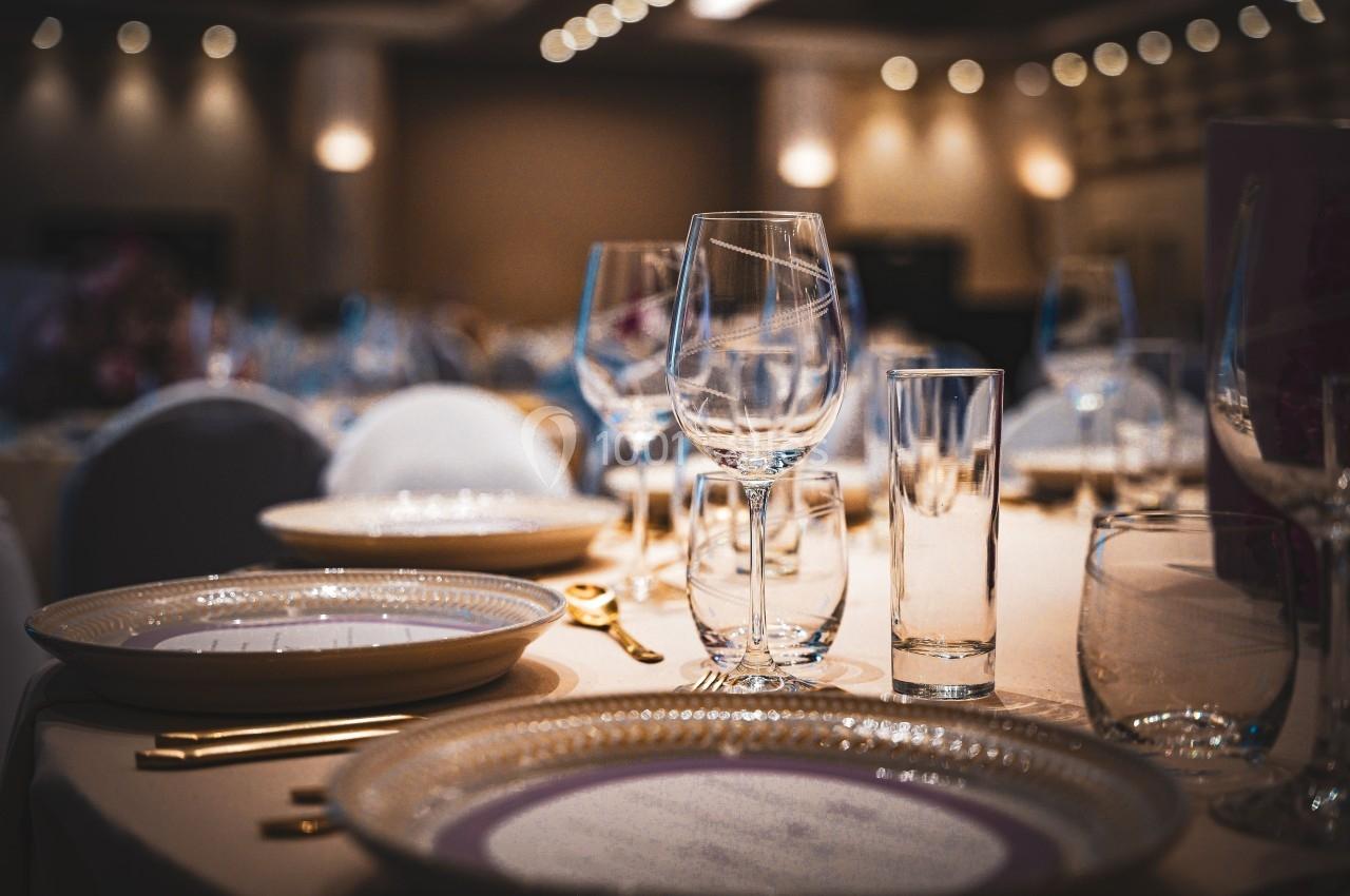 Table élégamment dressée avec assiettes, verres et couverts dorés dans une salle de réception éclairée.