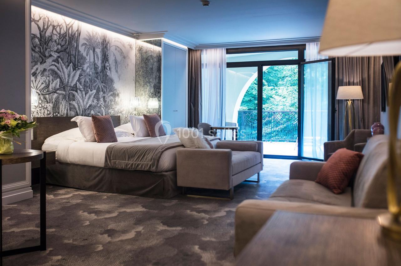 Chambre d'hôtel lumineuse avec lit double, canapé, table basse et grande baie vitrée donnant sur un balcon.